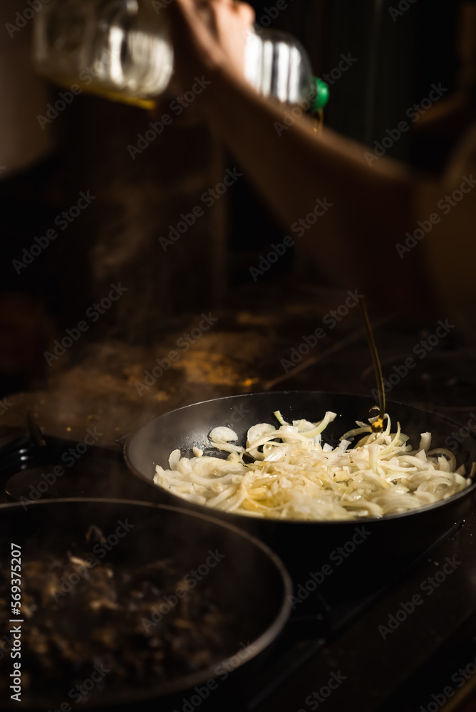Onions are fried in a pan and drizzled with olive oil. Dark background.