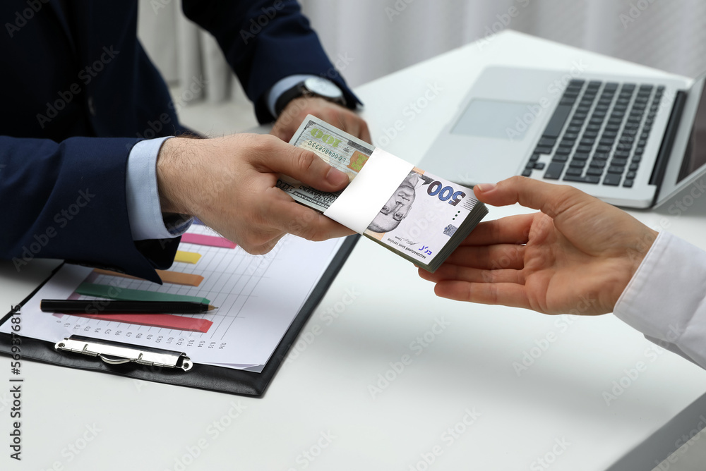 Currency exchange. Man giving money to woman at table, closeup. Combined hryvnia and dollar banknote design Currency exchange. Man giving money to woman at table, closeup. Combined hryvnia and dollar banknote design
