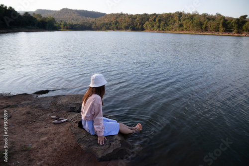 Women dressed in old-fashioned clothes sit with their feet in the water by the lake, feeling relaxed and reminiscent of nature.