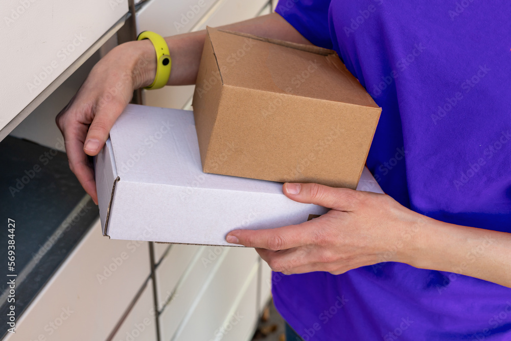 Person holding a cardboard box. A woman with a box in her hands near the self-service mail terminal. Parcel delivery machine. Mail delivery and post service, online shopping, e commerce concept Person holding a cardboard box. A woman with a box in her hands near the self-service mail terminal. Parcel delivery machine. Mail delivery and post service, online shopping, e commerce concept