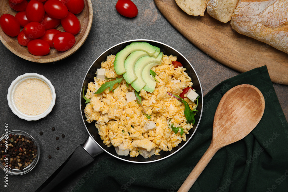 Frying pan with delicious scrambled eggs, tofu and avocado on black table, flat lay