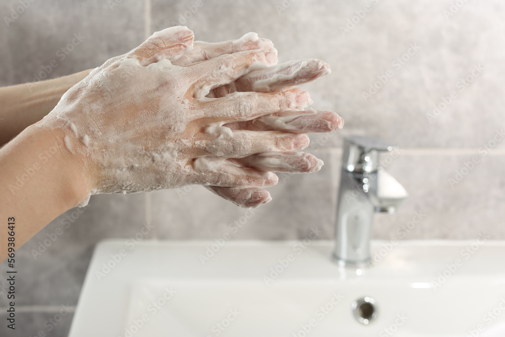 Woman washing hands with cleansing foam near sink in bathroom, closeup Woman washing hands with cleansing foam near sink in bathroom, closeup