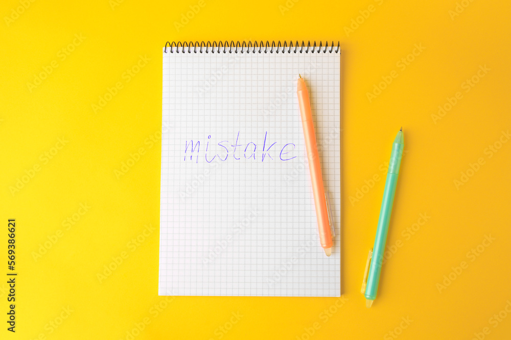 Word Mistake written in notepad with erasable pen on yellow background, flat lay Word Mistake written in notepad with erasable pen on yellow background, flat lay