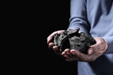 Man with handful of coal on dark background, closeup. Space for text
