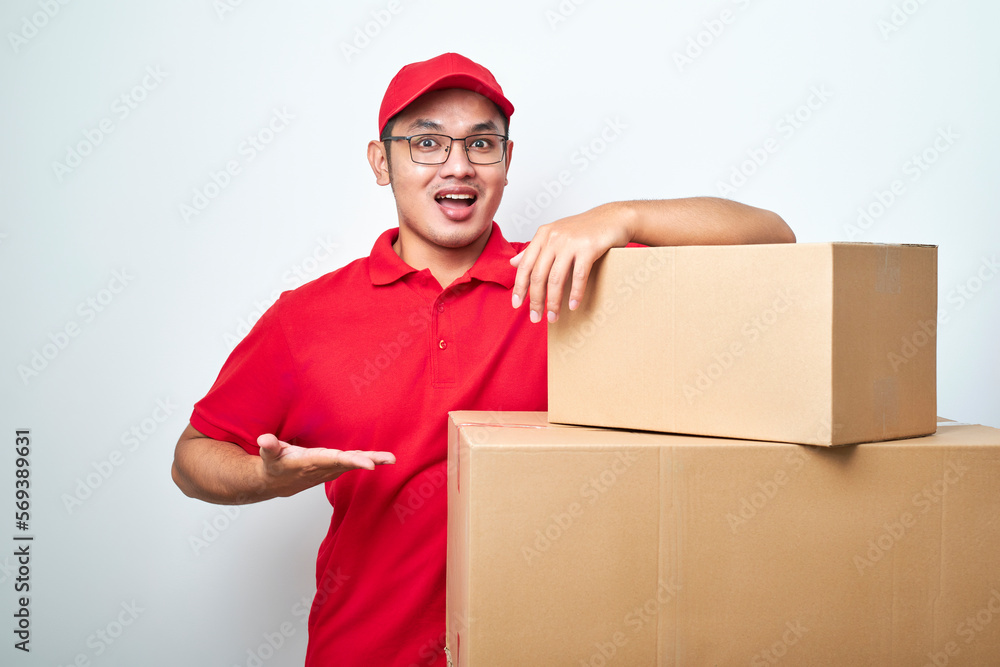 Confident asian courier man in red uniform encourage call service, showing and pointing at cardboard box while lean on it Confident asian courier man in red uniform encourage call service, showing and pointing at cardboard box while lean on it