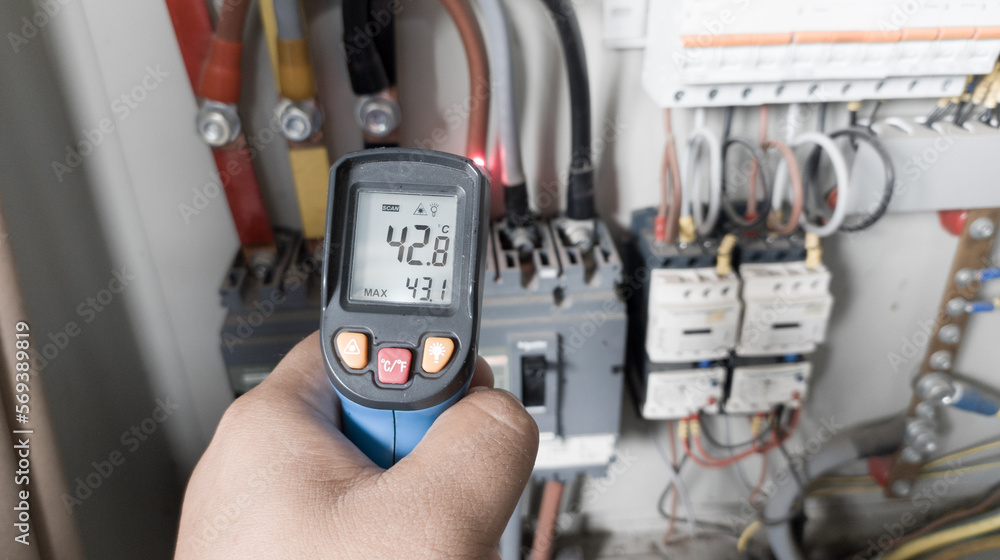 an electrician is using a thermogun to analyze sub-wires and components, to find out overcurrent loads, and abnormalities in the panel's electrical system.