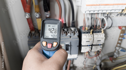 an electrician is using a thermogun to analyze sub-wires and components, to find out overcurrent loads, and abnormalities in the panel's electrical system.