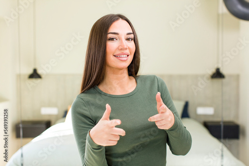 young adult pretty woman feeling happy, cool, satisfied, relaxed and successful, pointing at camera, choosing you photo