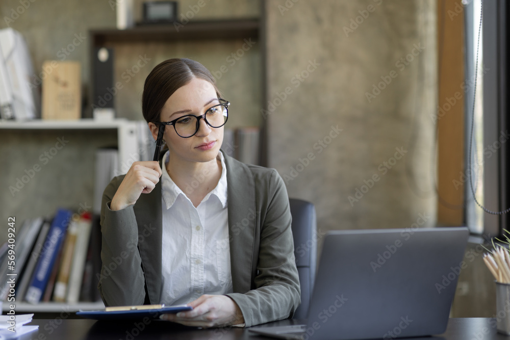 Fototapeta premium Portrait of smiling pretty young business woman in wearing glasses sitting on her workplace office, business finance concept.