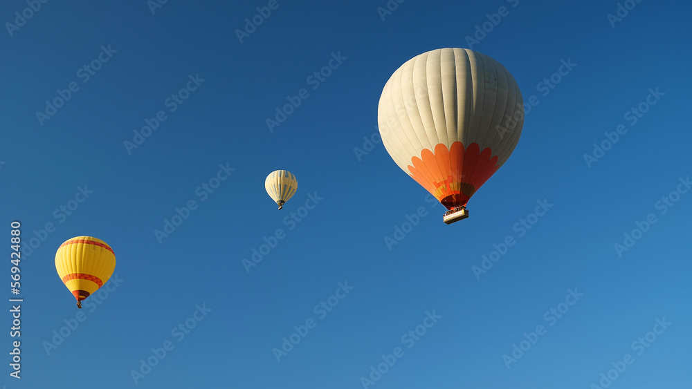 Naklejka premium Three hot air balloons with tourists against a blue cloudless sky. Beautiful view of colourful hot air balloons from below.