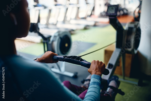 Close up of black sportswoman exercising on rowing machine in gym.