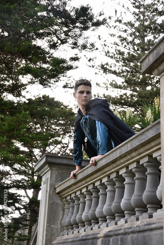 portrait of handsome man wearing fantasy medieval prince costume with golden crown and romantic silk shirt.  sitting on a stone balcony in a historical castle location background. photo