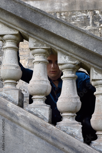 portrait of handsome man wearing fantasy medieval prince costume with golden crown and romantic silk shirt. sitting on a stone balcony in a historical castle location background.