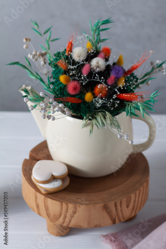 A small teapot is filled with a bouquet of dried flowers