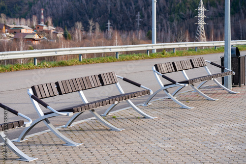 Wooden benches on the edge of the sidewalk near the parking lot in the amusement park. © Vectorina