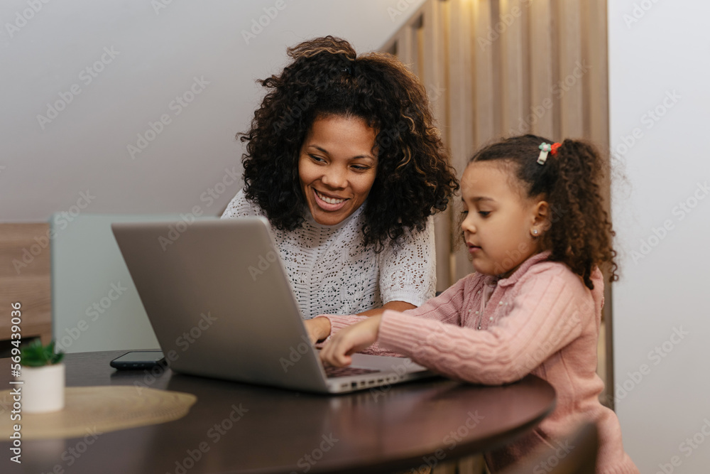 Happy family mother and child daughter at home working on the computer Happy family mother and child daughter at home working on the computer