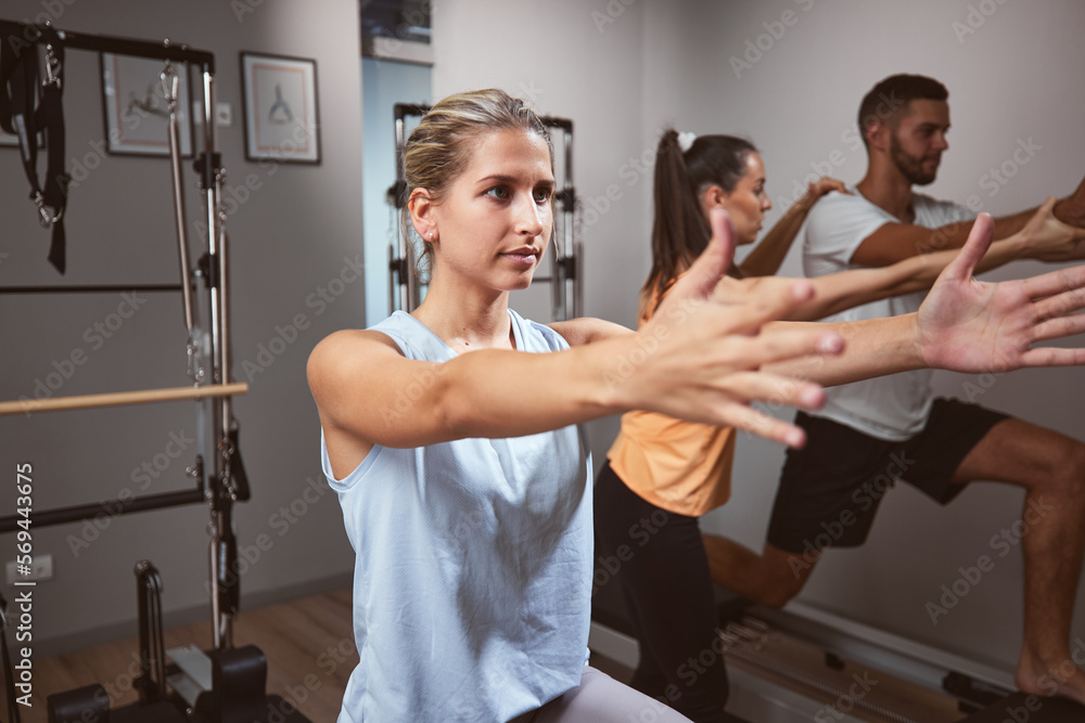 Young woman and man exercising in a gym with personal trainer on pilates machine. Young woman and man exercising in a gym with personal trainer on pilates machine.