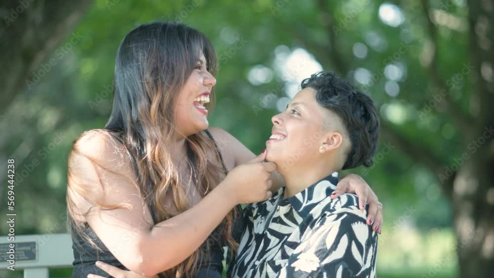 Latin lesbian couple intimately seated on park bench, symbolizing love, unity, and inclusiveness in the LGBTQ+ community. Slow-motion shots capture the tender moment between the couple.