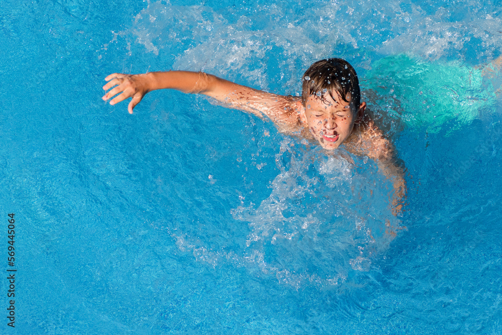 Child boy swim in blue water of hotel pool at summer resort. Kids fun leisure activity, wellness sport entertainment. Water sports and game, summer holiday, vacation concept. View from above