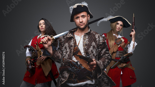 Shot of pirate man and two women with flintlock guns against grey background. © Fxquadro