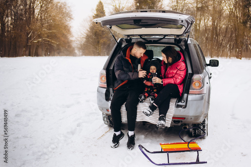 Happy family near car outdoors during snowfall. Winter vacation