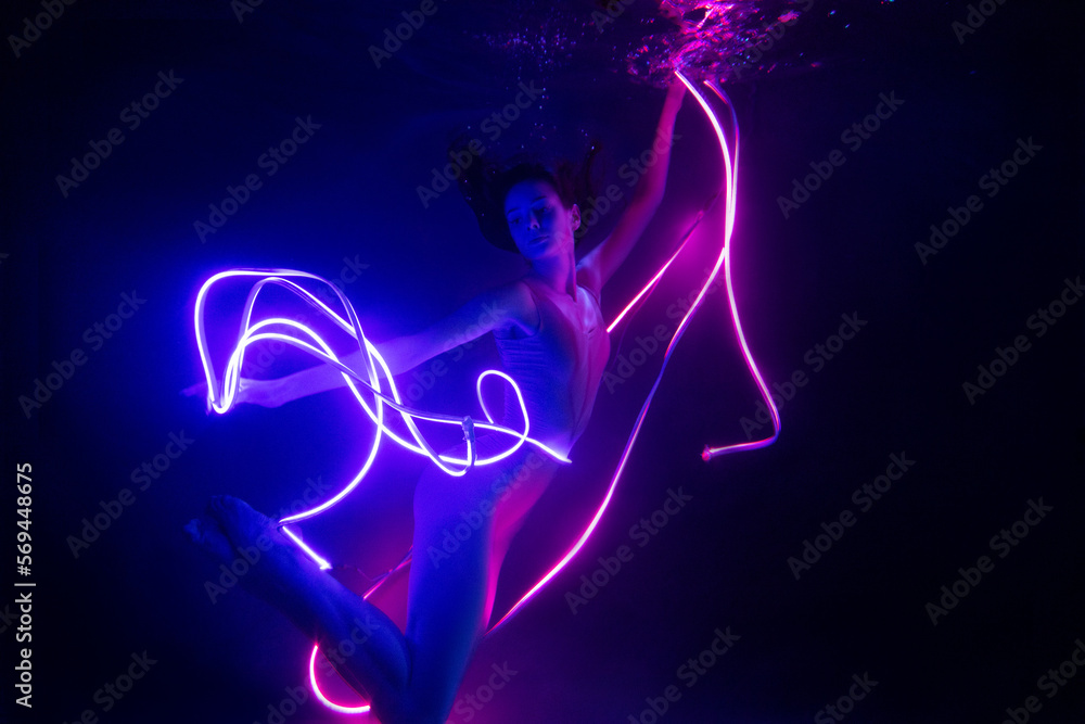 Gymnast shows underwater performance in neon light. Soft blurred focus Gymnast shows underwater performance in neon light. Soft blurred focus