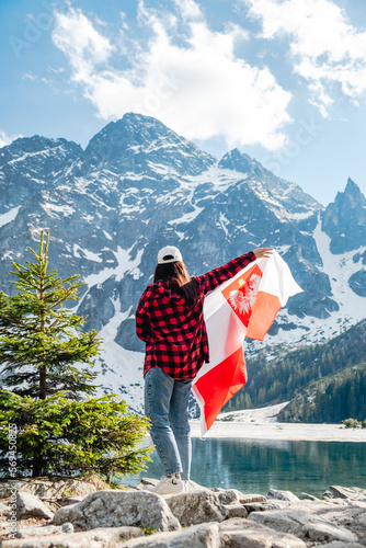 A woman with Poland flag is standing on the shore of a lake. Morskie Oko