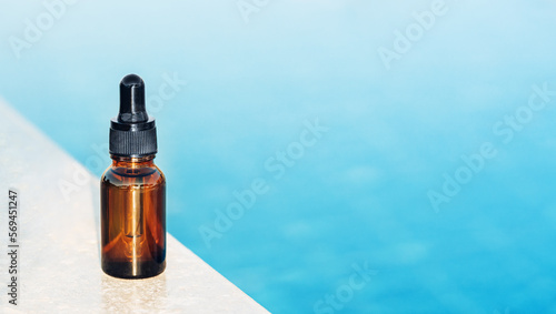 Natural medicine or essential aroma oil or beauty essence amber glass vial with dropper near blue water in sun. Face and body spa serum care concept banner. Hydration and moisturizer