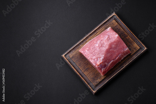 A piece of raw fresh pork on a wooden cutting board with spices and herbs