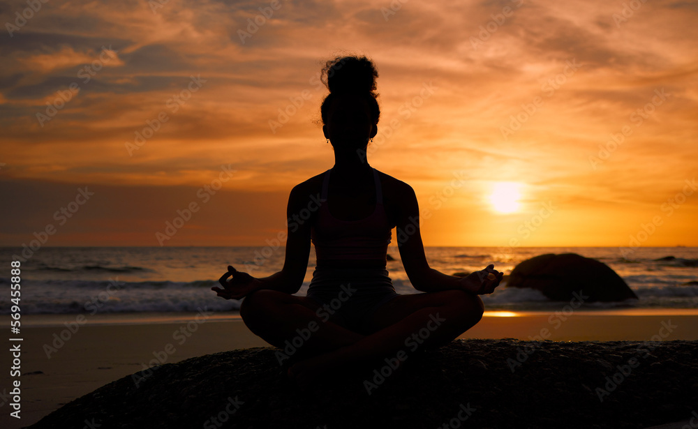 Sunset, beach and silhouette of a woman in a lotus pose while doing a yoga exercise by the sea. Peace, zen and shadow of a calm female doing meditation or pilates workout outdoor at dusk by the ocean