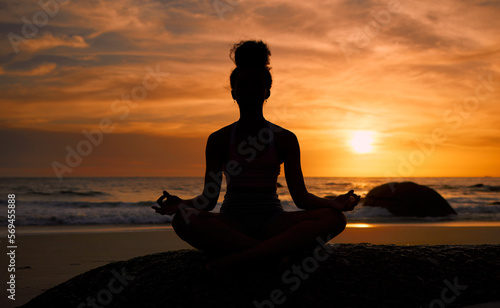 Sunset, beach and silhouette of a woman in a lotus pose while doing a yoga exercise by the sea. Peace, zen and shadow of a calm female doing meditation or pilates workout outdoor at dusk by the ocean © Lumeez/peopleimages.com