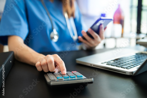 Healthcare costs and fees concept.Hand of smart doctor used a calculator and smartphone  tablet for medical costs at hospital in morning light.