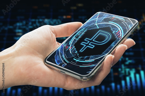 Close up of female hand holding cellphone with glowing blue ruble on dark background. Money, digital banking and finance concept.