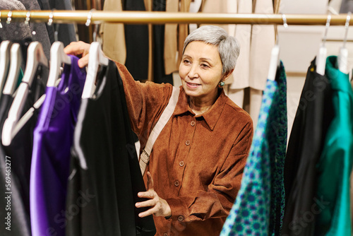 Of smiling senior woman browsing clothes on racks in boutique