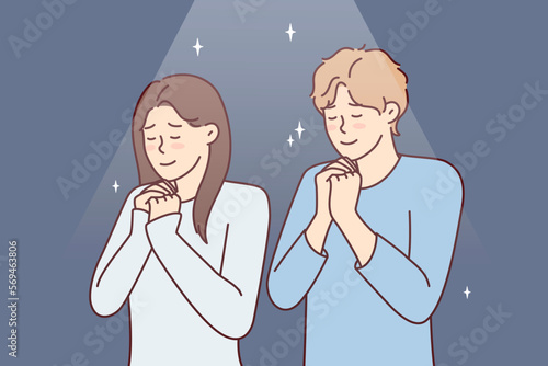 Positive man and woman praying asking god for happy marriage. Young couple stand with eyes closed and clasping palms in front of chest together performs religious ritual