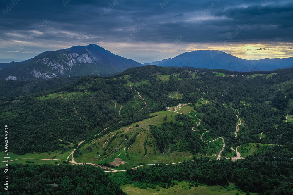 Aerial view of a beautiful landscape from Bucegi mountains in Romania, with forest green trees and cloudy sky. Travel to Romania.