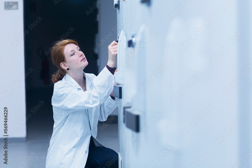 Young female engineer controlling a switch gear in control room, Freiburg im Breisgau, Baden-Württemberg, Germany Young female engineer controlling a switch gear in control room, Freiburg im Breisgau, Baden-Württemberg, Germany