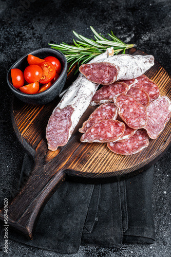 Spanish tapa Fuet sausage slices on wooden cutting board with herbs. Black background. Top view photo
