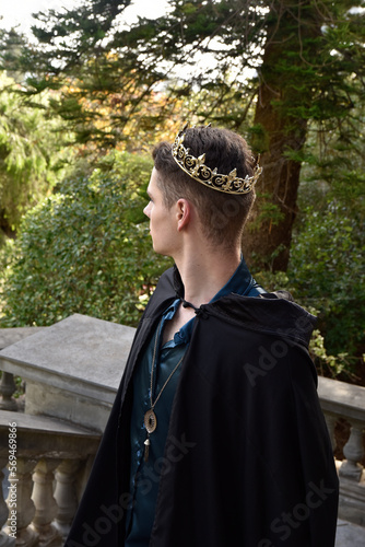 Close up portrait of handsome brunette man wearing fantasy medieval prince costume with golden crown and romantic silk shirt. historical castle location background. photo