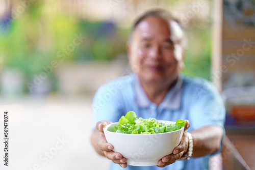 An elderly man holding a white bowl with lettuce. Healthy food concept.