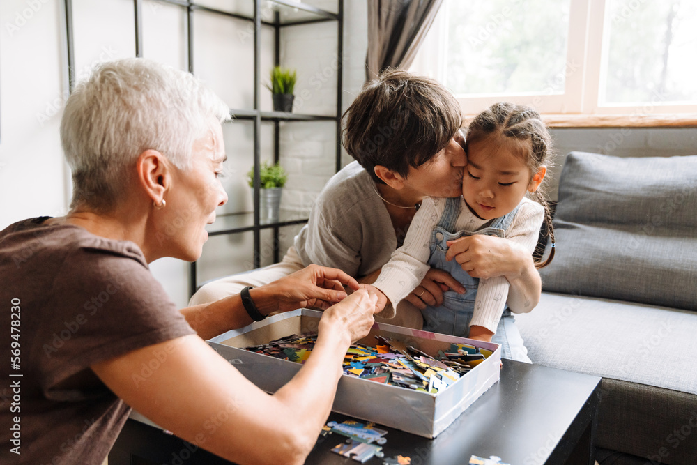 Obraz premium Grandmother kissing her little cute asian granddaughter holding puzzles