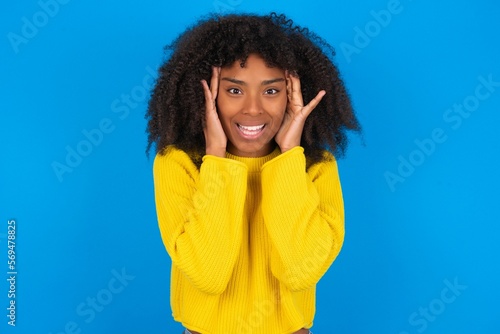 young woman with afro hairstyle wearing orange crop top over blue wall Pleasant looking cheerful  Happy reaction