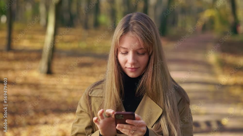 Front view of creative, young lady walking in park, standing, using smartphone. Attractive woman texting, scrolling, messaging, thinking, remembering. Concept of modern lifestyle. Front view of creative, young lady walking in park, standing, using smartphone. Attractive woman texting, scrolling, messaging, thinking, remembering. Concept of modern lifestyle.