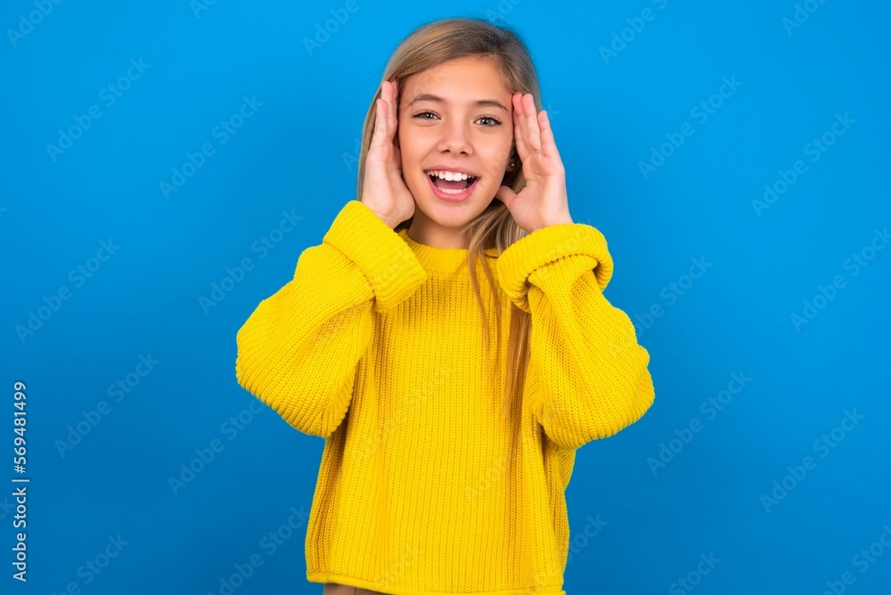 caucasian teen girl wearing yellow sweater over blue studio background Pleasant looking cheerful, Happy reaction caucasian teen girl wearing yellow sweater over blue studio background Pleasant looking cheerful, Happy reaction