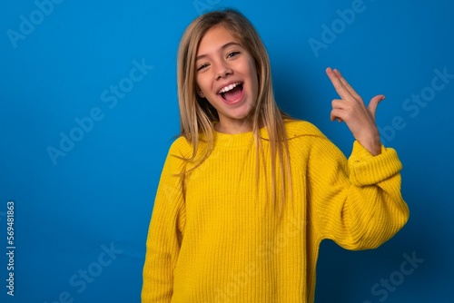 Quadro su tela caucasian teen girl wearing yellow sweater over blue studio background foolishness around shoots in temple with fingers makes suicide gesture