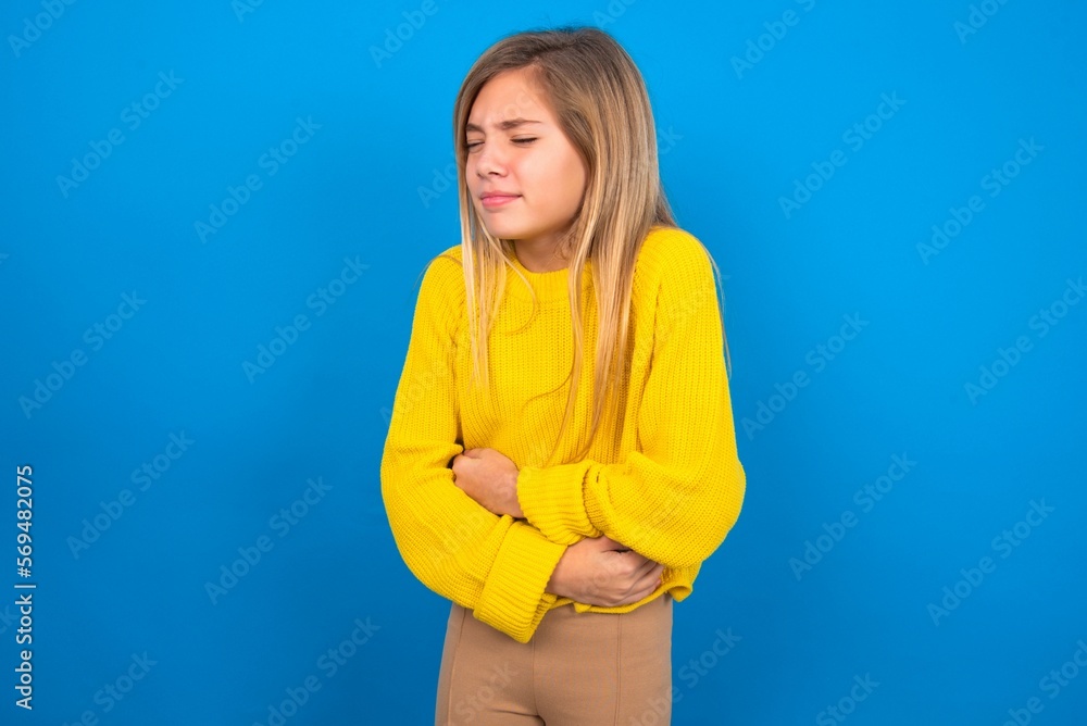caucasian teen girl wearing yellow sweater over blue studio background got stomachache caucasian teen girl wearing yellow sweater over blue studio background got stomachache