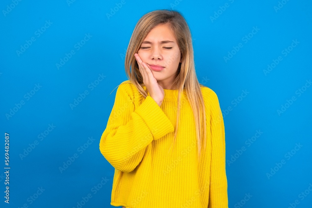 caucasian teen girl wearing yellow sweater over blue studio background with toothache caucasian teen girl wearing yellow sweater over blue studio background with toothache