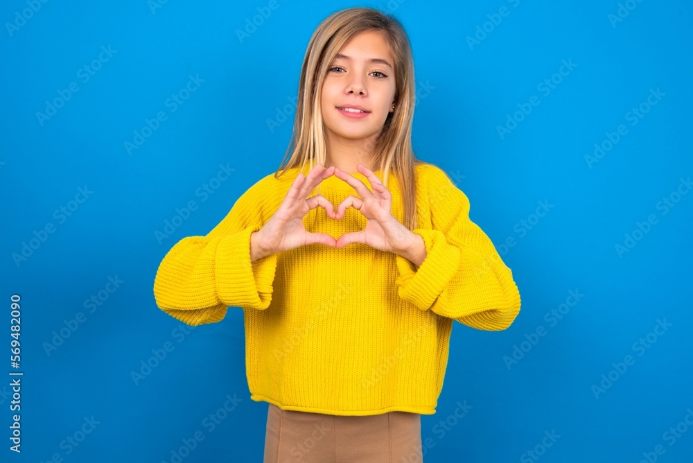 Serious caucasian teen girl wearing yellow sweater over blue studio background keeps hands crossed stands in thoughtful pose concentrated somewhere Serious caucasian teen girl wearing yellow sweater over blue studio background keeps hands crossed stands in thoughtful pose concentrated somewhere