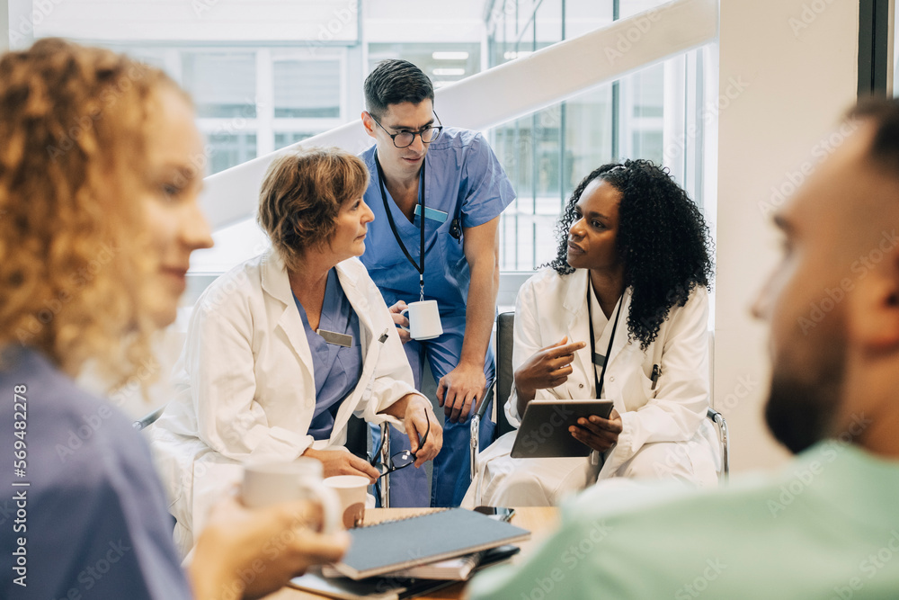Female doctor with tablet PC discussing with coworkers during coffee break at hospital Female doctor with tablet PC discussing with coworkers during coffee break at hospital