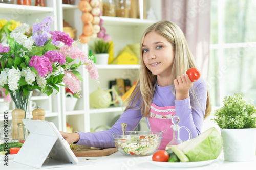 girl preparing fresh salad on kitchen table with tablet at home